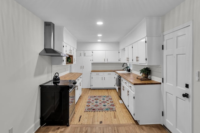 kitchen featuring light wood-style flooring, wooden counters, wall chimney exhaust hood, and a sink