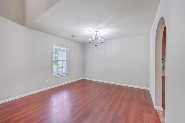 empty room featuring an inviting chandelier, arched walkways, dark wood-style floors, and baseboards