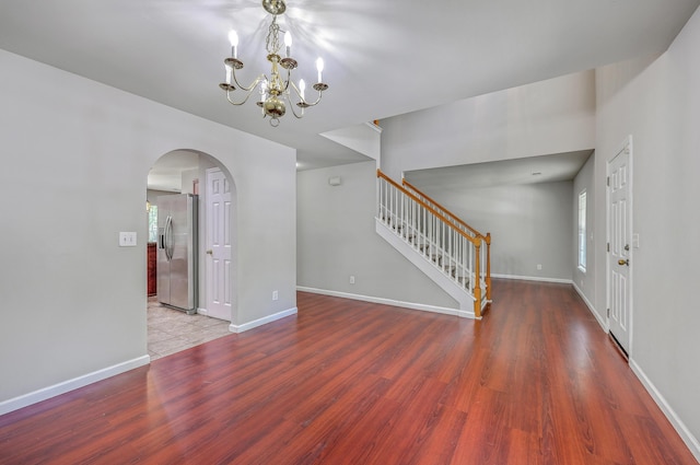 interior space with a chandelier, stairs, arched walkways, and wood finished floors