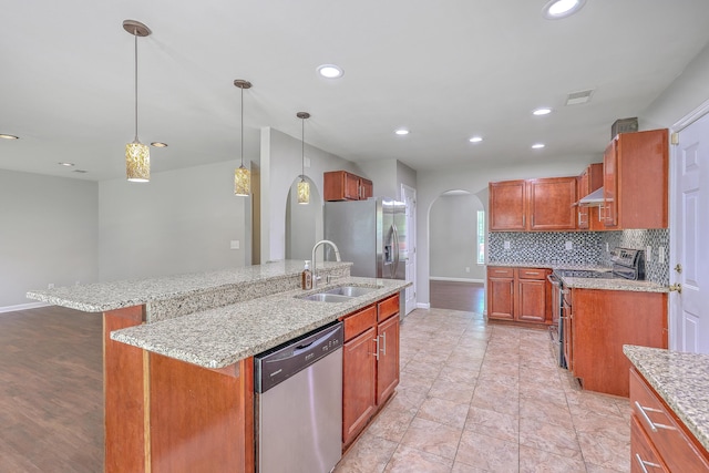 kitchen with a sink, under cabinet range hood, arched walkways, baseboards, and appliances with stainless steel finishes