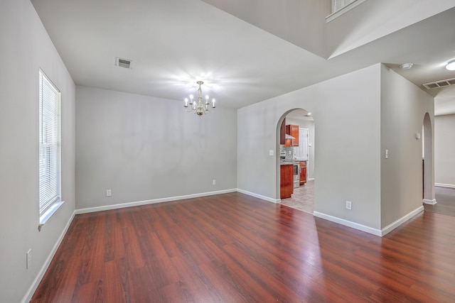 unfurnished room featuring dark wood finished floors, visible vents, and arched walkways