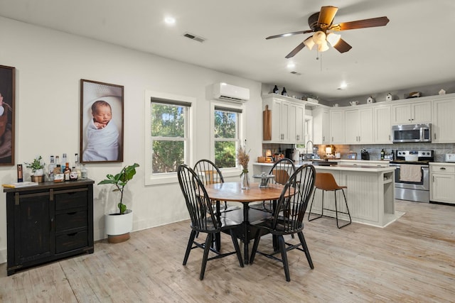 dining area featuring a wall unit AC, light wood-style floors, visible vents, and a ceiling fan