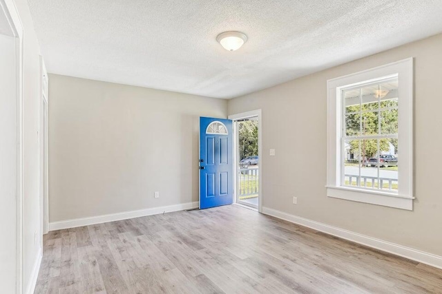 empty room featuring a textured ceiling, light wood finished floors, and baseboards