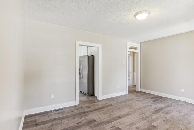 empty room with a textured ceiling, baseboards, and wood finished floors