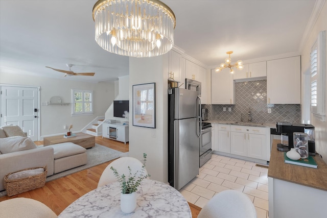 kitchen with light hardwood / wood-style flooring, decorative backsplash, white cabinets, ceiling fan with notable chandelier, and appliances with stainless steel finishes