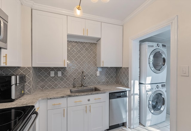 kitchen with sink, stacked washing maching and dryer, appliances with stainless steel finishes, white cabinets, and ornamental molding