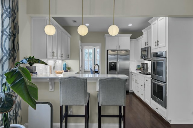 kitchen with a breakfast bar area, dark wood-type flooring, white cabinetry, stainless steel appliances, and decorative light fixtures