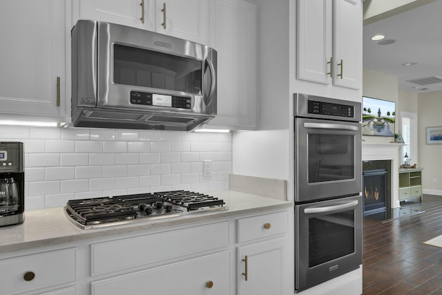 kitchen with stainless steel appliances, white cabinetry, light stone countertops, and decorative backsplash