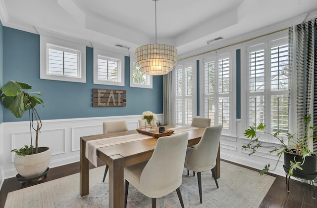 dining area with a raised ceiling, plenty of natural light, and dark hardwood / wood-style flooring