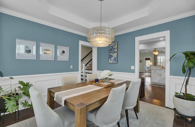 dining space featuring sink, an inviting chandelier, ornamental molding, a raised ceiling, and hardwood / wood-style floors