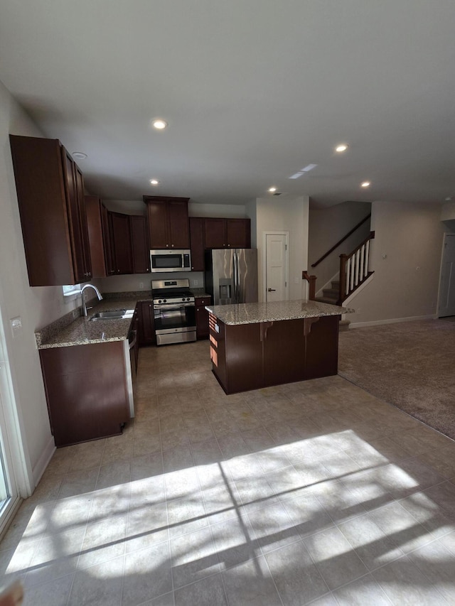 kitchen with appliances with stainless steel finishes, a kitchen island, a sink, and baseboards