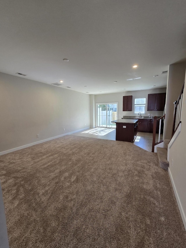 interior space featuring light carpet, a sink, visible vents, baseboards, and stairway