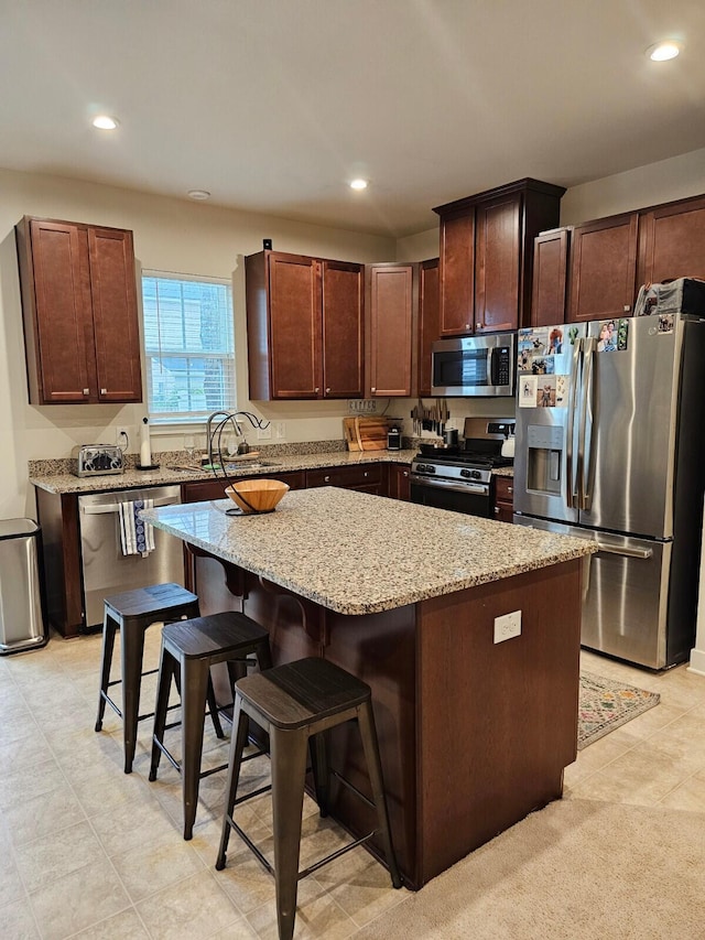 kitchen with stainless steel appliances, a kitchen island, a sink, light stone countertops, and a kitchen bar