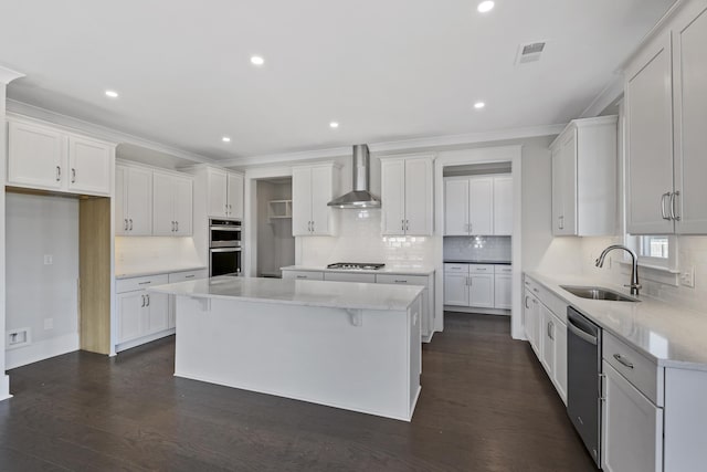 kitchen with appliances with stainless steel finishes, sink, white cabinets, a center island, and wall chimney exhaust hood