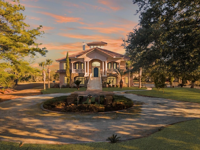 mediterranean / spanish-style home featuring a tiled roof, a front lawn, curved driveway, and stucco siding