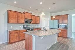 kitchen with appliances with stainless steel finishes, light stone countertops, hanging light fixtures, hardwood / wood-style flooring, and an island with sink