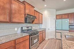 kitchen featuring light hardwood / wood-style floors, stainless steel range oven, white refrigerator, and light stone countertops