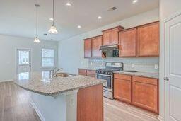 kitchen with a center island with sink, sink, pendant lighting, light hardwood / wood-style flooring, and stainless steel electric range oven