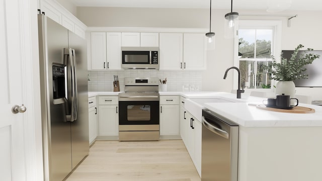 kitchen featuring light wood finished floors, stainless steel appliances, decorative backsplash, white cabinets, and a sink