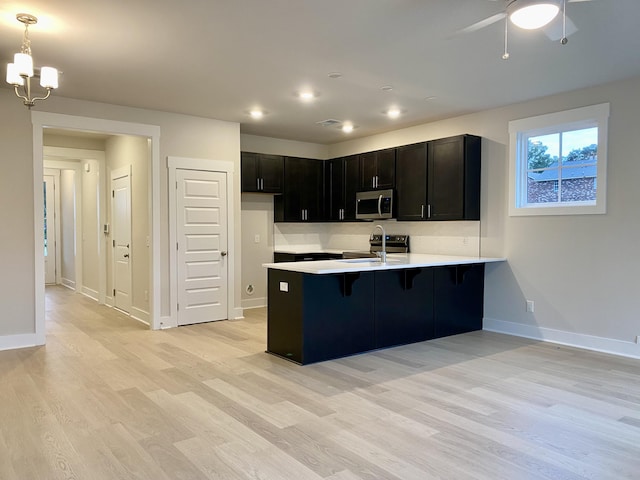 kitchen featuring appliances with stainless steel finishes, a peninsula, light countertops, light wood-type flooring, and a sink