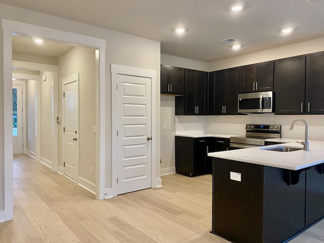 kitchen with stainless steel appliances, a sink, visible vents, and light wood-style floors