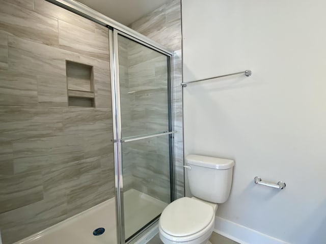 full bath featuring toilet, a shower stall, and baseboards