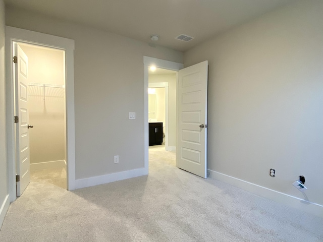 unfurnished bedroom featuring light carpet, baseboards, visible vents, and a walk in closet