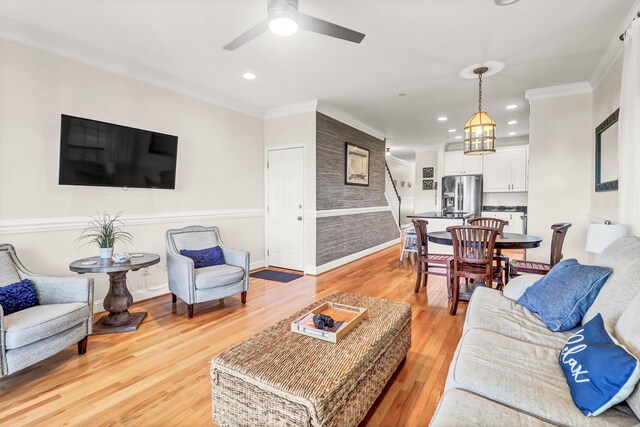 living area featuring light wood-type flooring, ornamental molding, ceiling fan with notable chandelier, recessed lighting, and baseboards