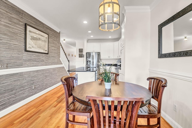 dining space featuring light wood finished floors, recessed lighting, an accent wall, and ornamental molding