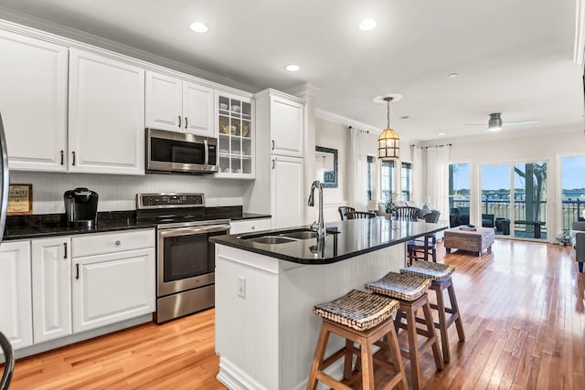 kitchen featuring light wood finished floors, a kitchen bar, white cabinets, stainless steel appliances, and a sink