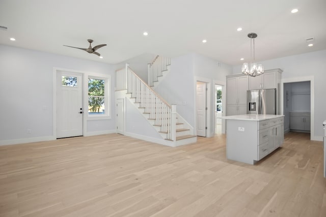 interior space featuring pendant lighting, a center island, ceiling fan with notable chandelier, stainless steel refrigerator with ice dispenser, and light hardwood / wood-style flooring