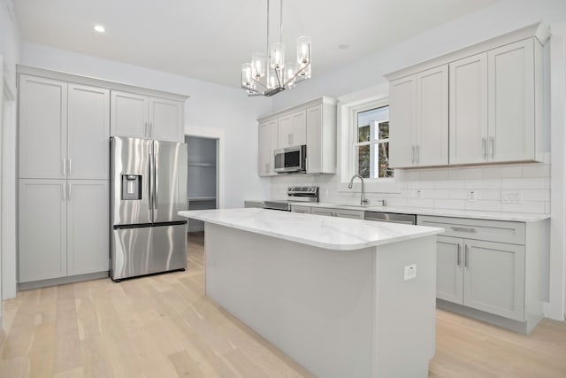 kitchen with appliances with stainless steel finishes, decorative backsplash, light hardwood / wood-style floors, a kitchen island, and a chandelier