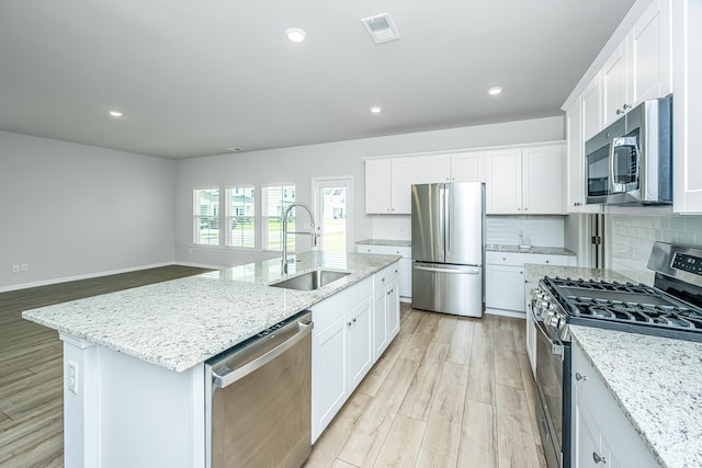 kitchen with appliances with stainless steel finishes, tasteful backsplash, white cabinets, light hardwood / wood-style floors, and an island with sink