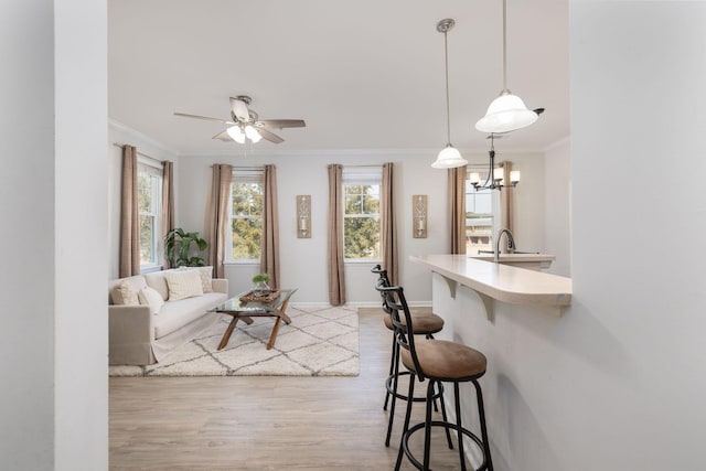 living room featuring light wood finished floors, ceiling fan, ornamental molding, and baseboards