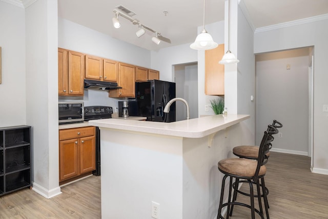 kitchen featuring light wood-style floors, a kitchen breakfast bar, a peninsula, under cabinet range hood, and black appliances