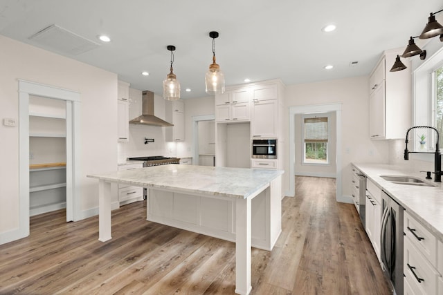 kitchen featuring wall chimney exhaust hood, a kitchen island, decorative light fixtures, white cabinetry, and a sink