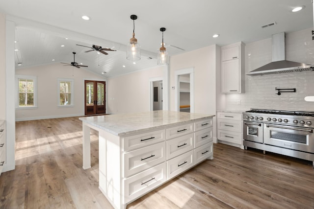 kitchen featuring range with two ovens, wall chimney exhaust hood, open floor plan, a center island, and white cabinetry