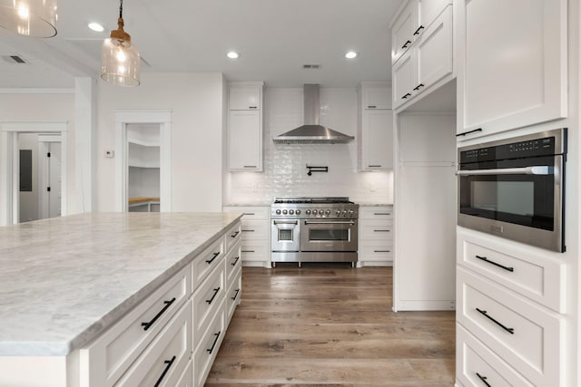 kitchen with appliances with stainless steel finishes, white cabinetry, wall chimney range hood, and decorative light fixtures