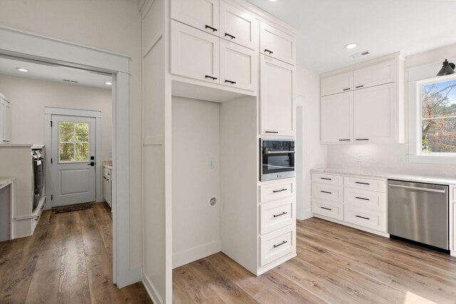 kitchen with appliances with stainless steel finishes, a healthy amount of sunlight, light countertops, and white cabinetry