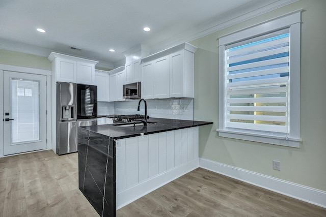 kitchen with appliances with stainless steel finishes, white cabinetry, decorative backsplash, crown molding, and light wood-type flooring