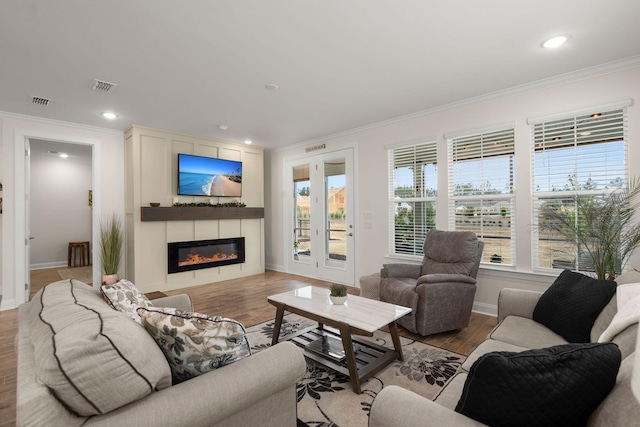 living room featuring wood finished floors, visible vents, baseboards, ornamental molding, and a glass covered fireplace