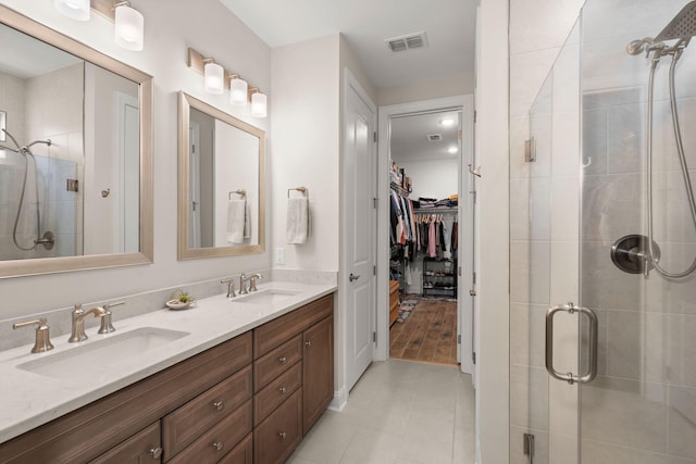 full bathroom with double vanity, a sink, visible vents, and a shower stall