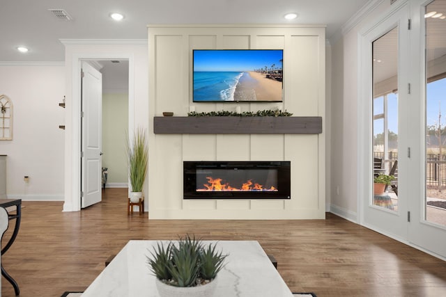 living room with wood finished floors, a glass covered fireplace, and crown molding