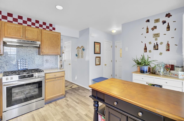 kitchen with tasteful backsplash, under cabinet range hood, light wood-type flooring, light countertops, and gas stove