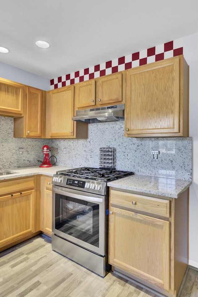 kitchen with light stone counters, gas stove, decorative backsplash, light wood-style floors, and under cabinet range hood