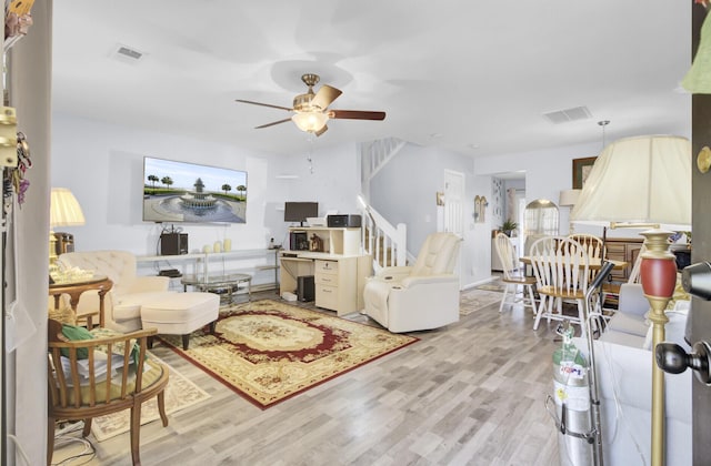 living area featuring ceiling fan, stairway, visible vents, and light wood-type flooring