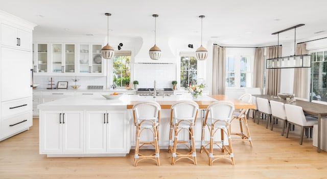 202 Bank St, Mount Pleasant, SC 29464 - kitchen with backsplash, white cabinetry, light countertops, a center island with sink, and light wood-type flooring