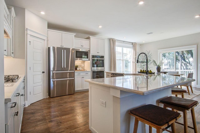 kitchen with a center island with sink, white cabinets, dark hardwood / wood-style floors, and appliances with stainless steel finishes