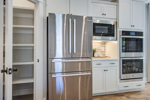 kitchen featuring stainless steel appliances, white cabinetry, decorative backsplash, and wood-type flooring