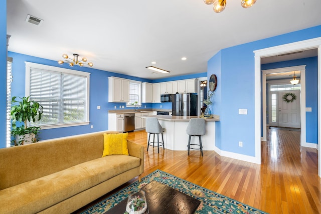living room with light wood-style floors, baseboards, a notable chandelier, and visible vents